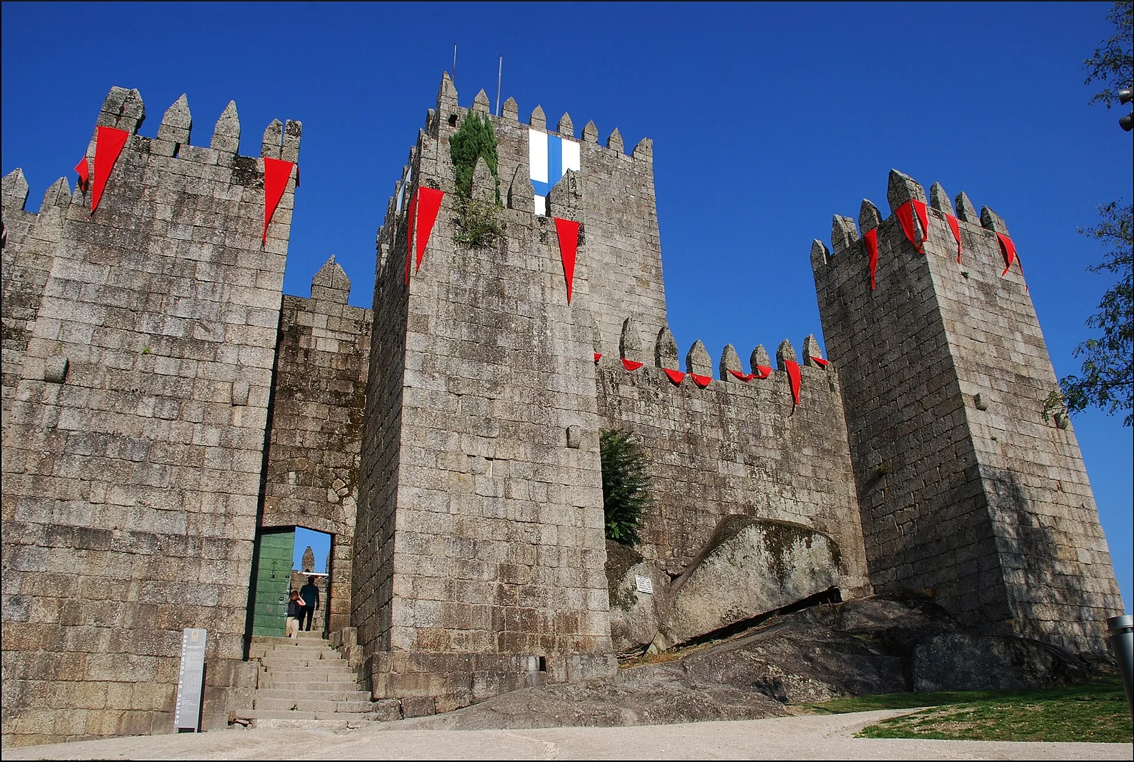 Stone walls and towers of Guimarães Castle on a green hill.