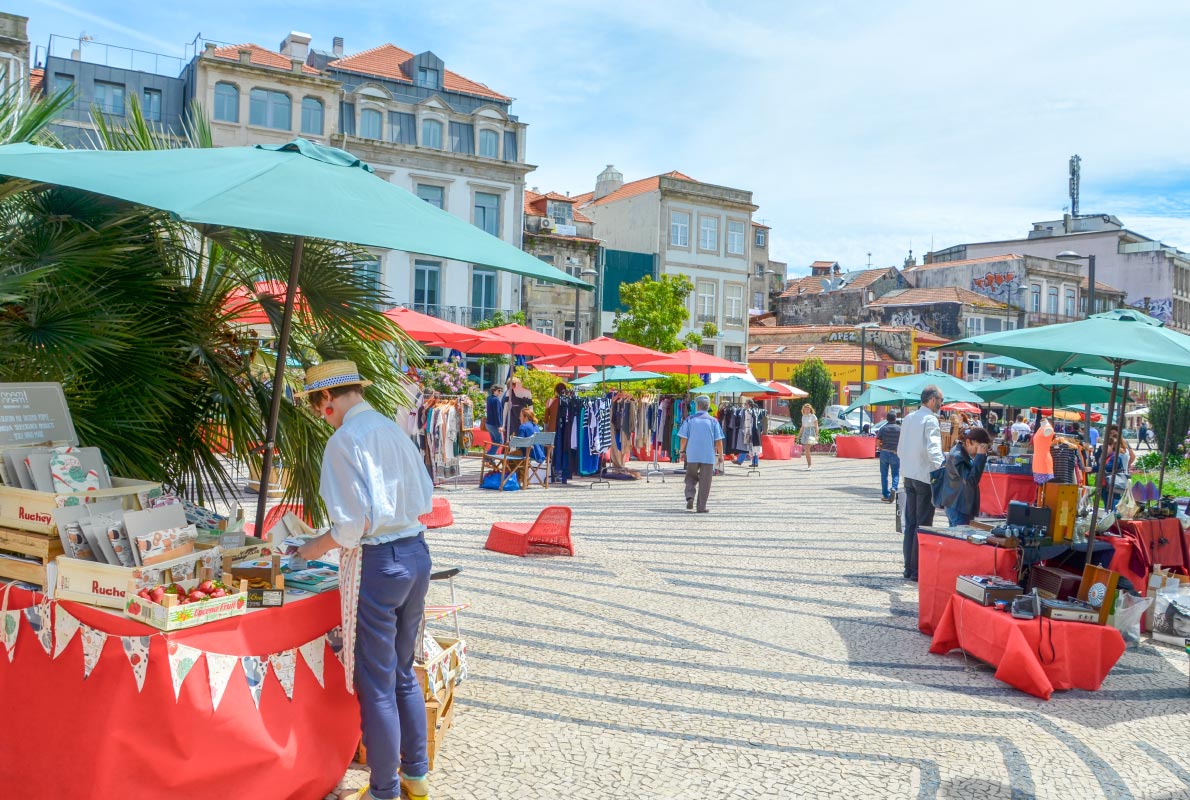 Mercado Porto Belo stalls with clothing, books, and design items around Praca Carlos Alberto.