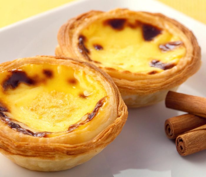 Two pastel de nata custard tarts on a plate with cinnamon sticks.