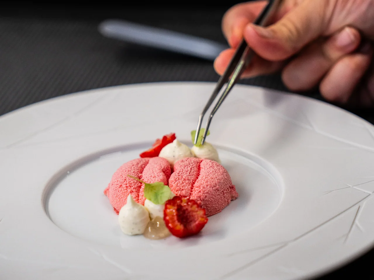 A pink dessert with fresh strawberry being finished with tweezers at Antiqvvm.